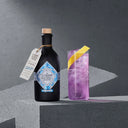 The Illusionist Masquerade Alcohol-Free Bottle Next to Pink Cocktail in a Glass